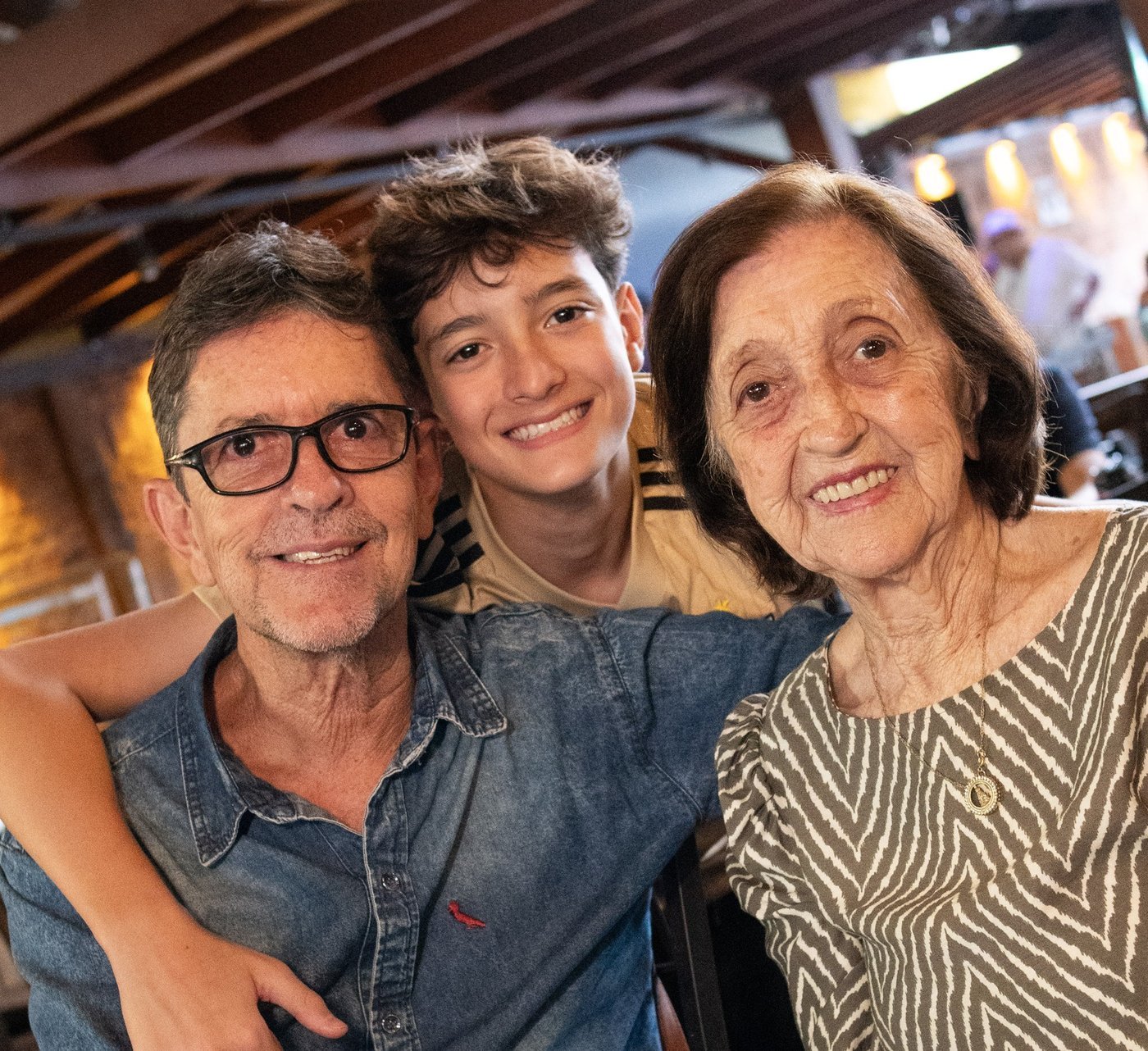 Avô, neto e avó sorrindo à mesa do Boi Vindo, três gerações reunidas